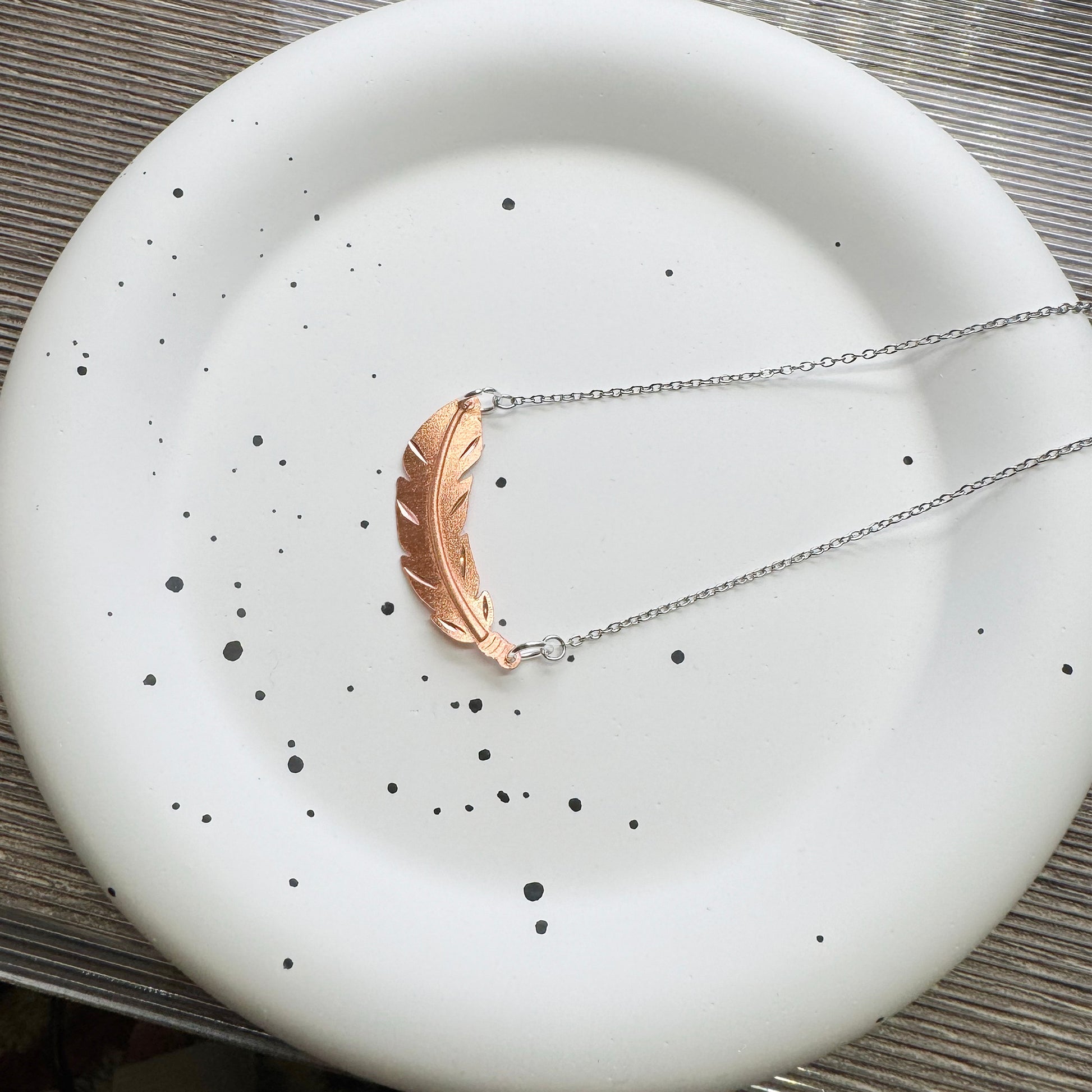 Unisex feather necklace on 18-inch stainless steel chain, displayed on wood