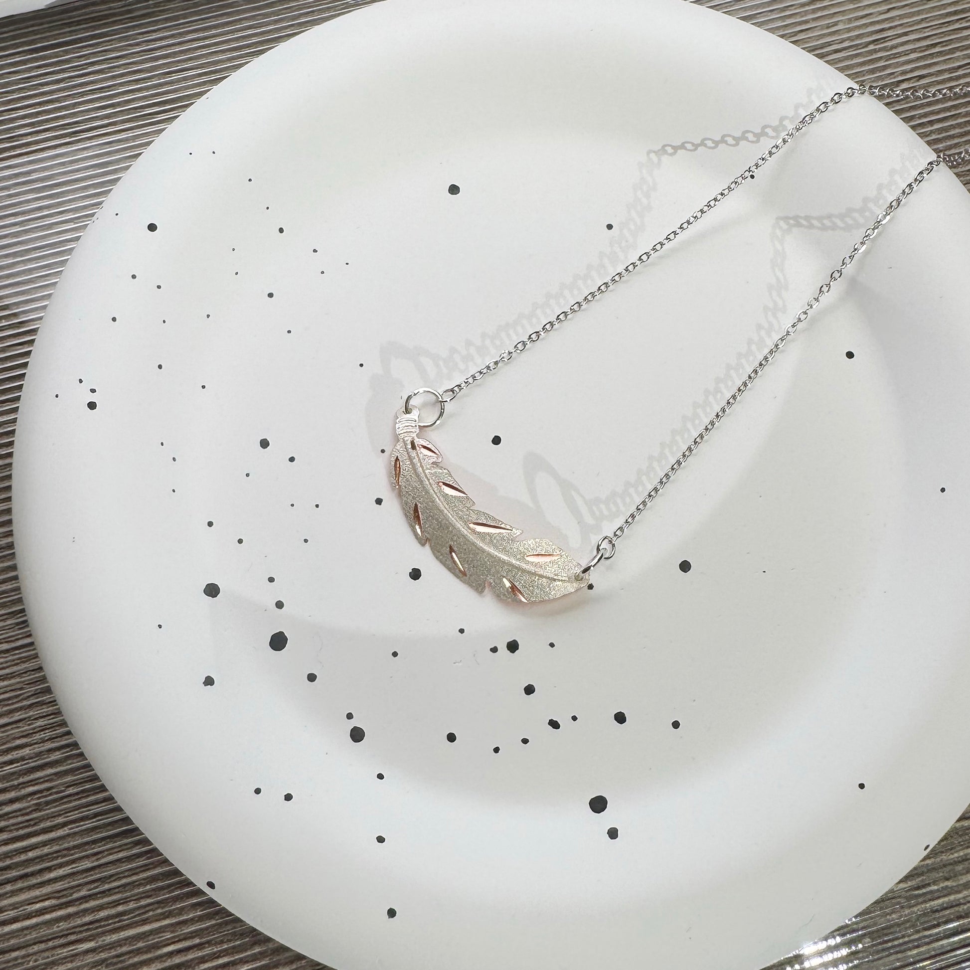 Close-up of silver color feather pendant with artistic copper background
